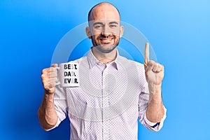 Young handsome bald man drinking cup of coffee with best dad ever message smiling with an idea or question pointing finger with