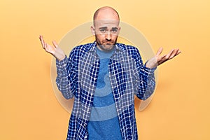 Young handsome bald man wearing casual shirt clueless and confused with open arms, no idea and doubtful face