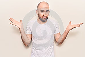 Young handsome bald man wearing casual t shirt clueless and confused with open arms, no idea and doubtful face