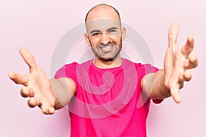 Young handsome bald man wearing casual t shirt looking at the camera smiling with open arms for hug