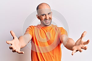 Young handsome bald man wearing casual t shirt looking at the camera smiling with open arms for hug