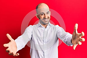 Young handsome bald man wearing elegant shirt looking at the camera smiling with open arms for hug