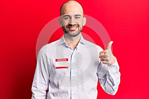 Young handsome bald man wearing hello my name is sticker smiling happy and positive, thumb up doing excellent and approval sign