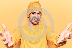 Young handsome bald man wearing sweater and wool cap looking at the camera smiling with open arms for hug
