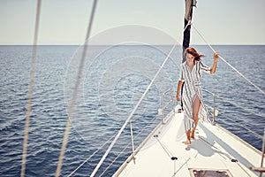 A young handsome barefoot female model standing on the bow of a yacht on the sea and enjoying the sun and the wind. Summer, sea,
