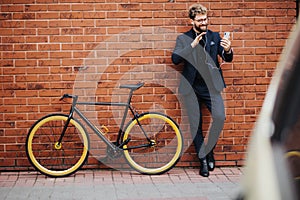 Young handsome bearded business man with earbeans talking on the phone on video call with hello gesture standing near his bicycle