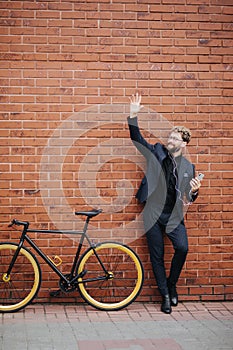 Young handsome bearded business man in suit and glasses wave with hands hello gesture for greatings standing near his bicycle on