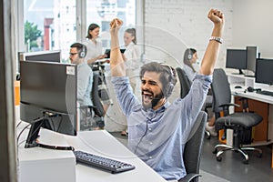 Young handsome bearded businessman celebrating corporate success with his fists raised in the air