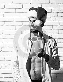 Young handsome bearded christmas man with stylish beard in red santa claus hat and white shirt with muscular bare
