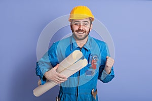 Young handsome bearded man engineer, architect holding rolled up technical drawing, looks happy, celebrating succses of new