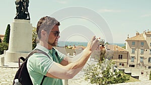 Young handsome bearded man making outdoor photos with his compact camera