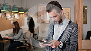 Young handsome bearded man uses touchscreen tablet in the modern startup office.