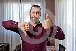 Young handsome bearded man wearing purple shirt doing thumbs up and down, disagree and agree expression