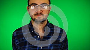 Young handsome bearded white man in glasses against green background