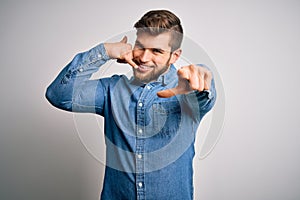 Young handsome blond man with beard and blue eyes wearing casual denim shirt smiling doing talking on the telephone gesture and