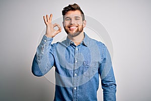 Young handsome blond man with beard and blue eyes wearing casual denim shirt smiling positive doing ok sign with hand and fingers