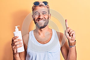 Young handsome blond man with beard on vacation holding bottle of sunscreen to protect skin smiling with an idea or question