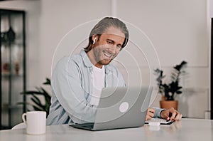 young handsome blond man with a laptop at his desk studying remotely and taking notes. student dressed in casual with