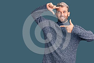 Young handsome blond man wearing casual sweater smiling making frame with hands and fingers with happy face