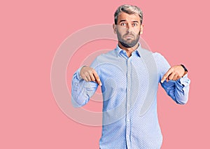 Young handsome blond man wearing elegant shirt pointing down looking sad and upset, indicating direction with fingers, unhappy and