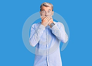 Young handsome blond man wearing elegant shirt shocked covering mouth with hands for mistake