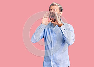 Young handsome blond man wearing elegant shirt shouting angry out loud with hands over mouth