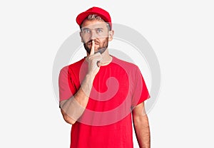 Young handsome blond man wearing t-shirt and cap asking to be quiet with finger on lips