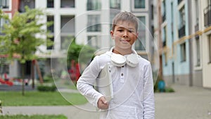 Young Handsome Boy Standing on the Street and Holding a Laptop and Wearing Headphones.