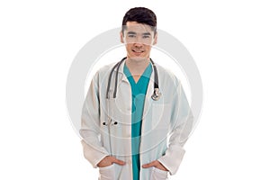 Young handsome brunette man doctor in uniform with stethoscope on his shoulders looking and smiling on camera isolated