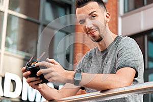 Young Handsome Brunette Man Launching Drone Quadcopter and Holding Joystick Remote Controller. Man Looking At Camera