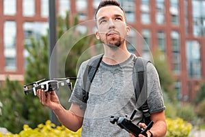 Young Handsome Brunette Man Launching Drone Quadcopter and Looking Above Viewer. Urban Stlilysh Contemporary Cityscape