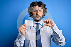 Young handsome business man with beard holding id card identification over blue background with angry face, negative sign showing