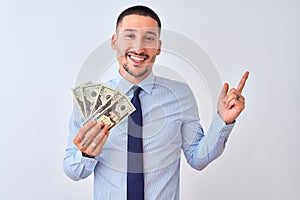 Young handsome business man holding a bunch of bank notes dollars over isolated background very happy pointing with hand and