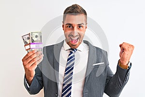 Young handsome business man holding bunch of dollars banknotes over isolated background screaming proud and celebrating victory