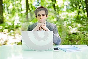 Young handsome business man over laptop at office table look at camera in green park. Business concept.