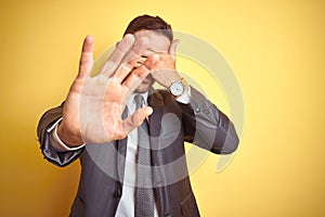 Young handsome business man over yellow isolated background covering eyes with hands and doing stop gesture with sad and fear
