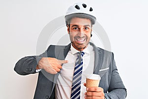 Young handsome business man wearing bike helmet and take away coffee over isolated background with surprise face pointing finger