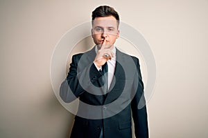 Young handsome business man wearing elegant suit and tie over isolated background asking to be quiet with finger on lips