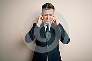 Young handsome business man wearing elegant suit and tie over isolated background covering ears with fingers with annoyed