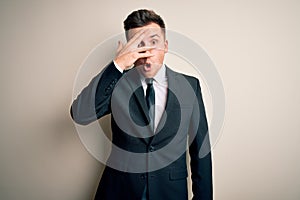 Young handsome business man wearing elegant suit and tie over isolated background peeking in shock covering face and eyes with