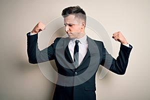 Young handsome business man wearing elegant suit and tie over isolated background showing arms muscles smiling proud