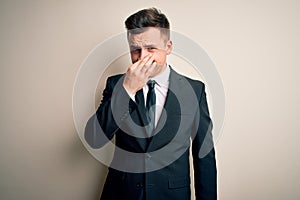 Young handsome business man wearing elegant suit and tie over isolated background smelling something stinky and disgusting,