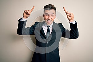 Young handsome business man wearing elegant suit and tie over isolated background smiling amazed and surprised and pointing up