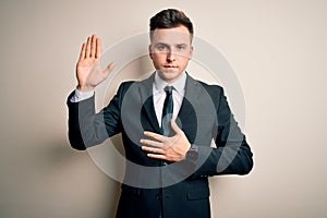 Young handsome business man wearing elegant suit and tie over isolated background Swearing with hand on chest and open palm,