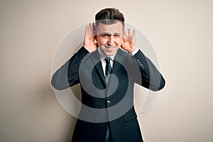 Young handsome business man wearing elegant suit and tie over isolated background Trying to hear both hands on ear gesture,