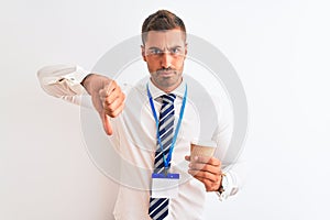 Young handsome business man wearing id pass and drinking coffee over isolated background with angry face, negative sign showing