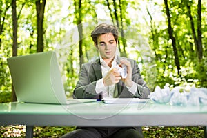 Young handsome business man at work table office with laptop in green forest with crumpled papers blank . Business concept