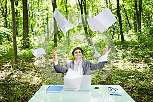 Young handsome business man at work table office with laptop in green forest with fly papers blank. Business concept