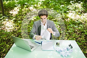 Young handsome business man at work table office with laptop in green forest tear work papers. Business concept