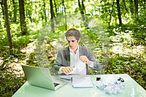 Young handsome business man at work table office with laptop in green forest tear work papers. Business concept